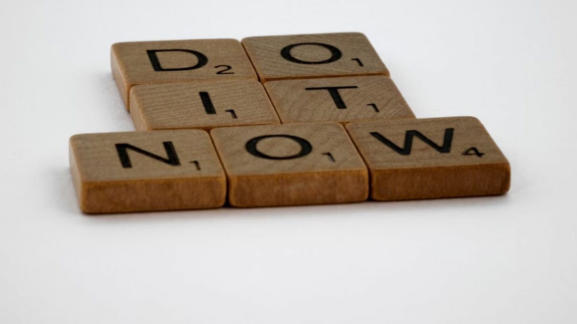 Wooden Scrabble tiles spelling 'Do It Now' on a white background. Motivational concept.