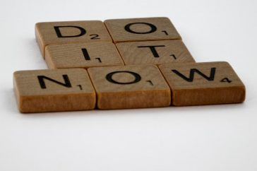 Wooden Scrabble tiles spelling 'Do It Now' on a white background. Motivational concept.