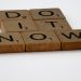 Wooden Scrabble tiles spelling 'Do It Now' on a white background. Motivational concept.
